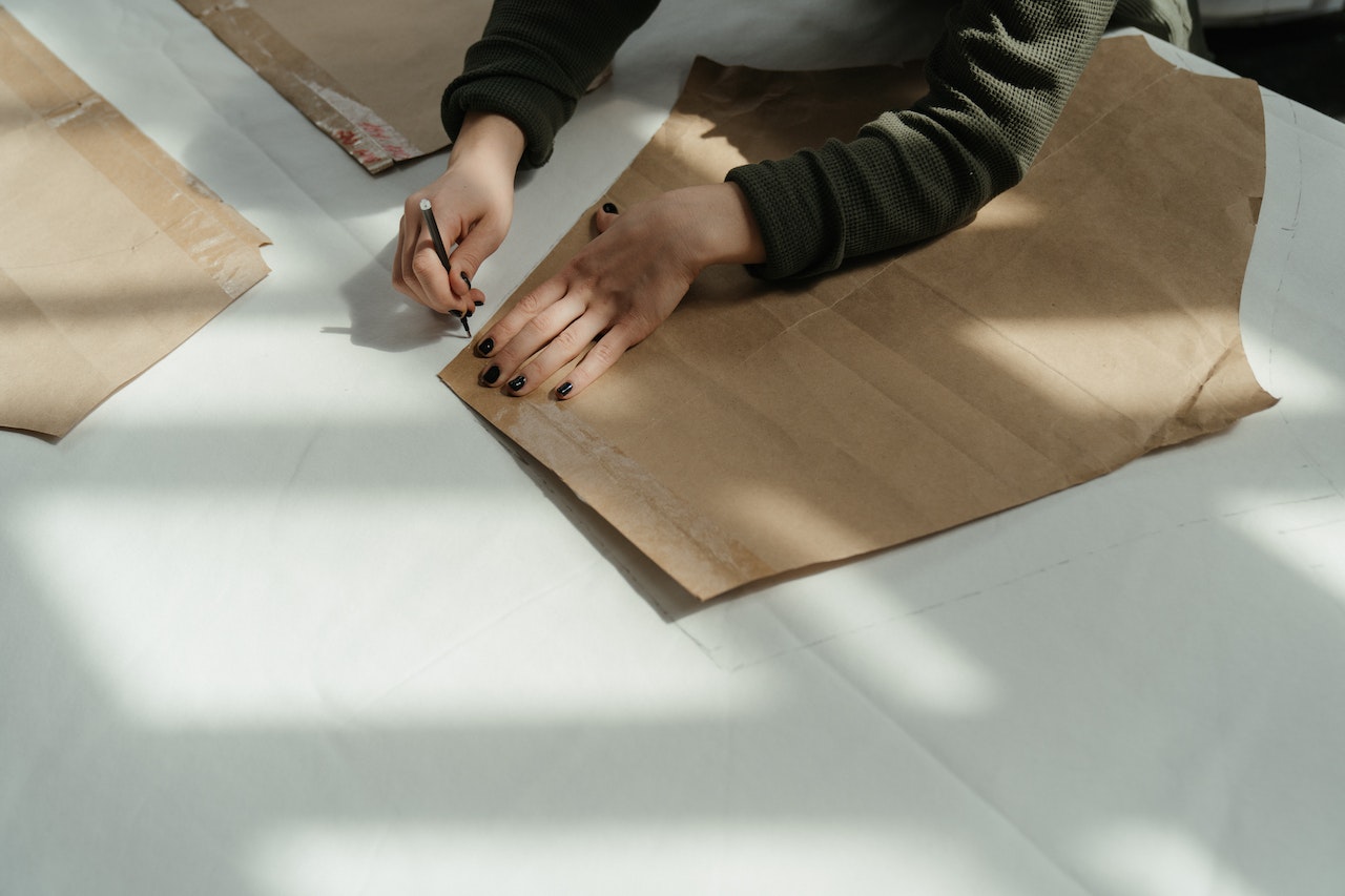 person cutting paper pattern for clothing on a table