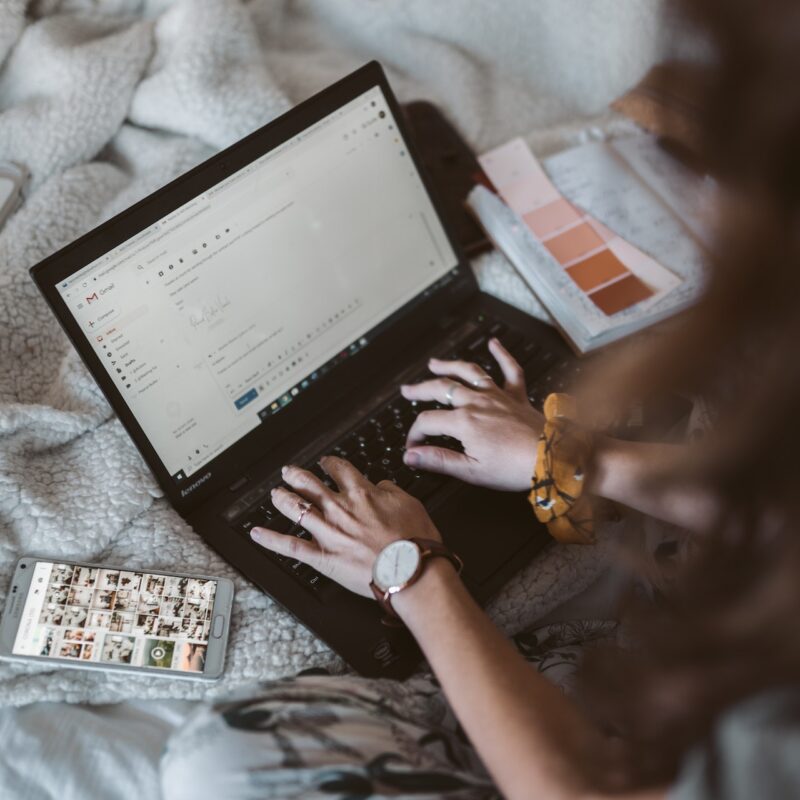 marketer designing emails on a laptop with a cell phone next to her