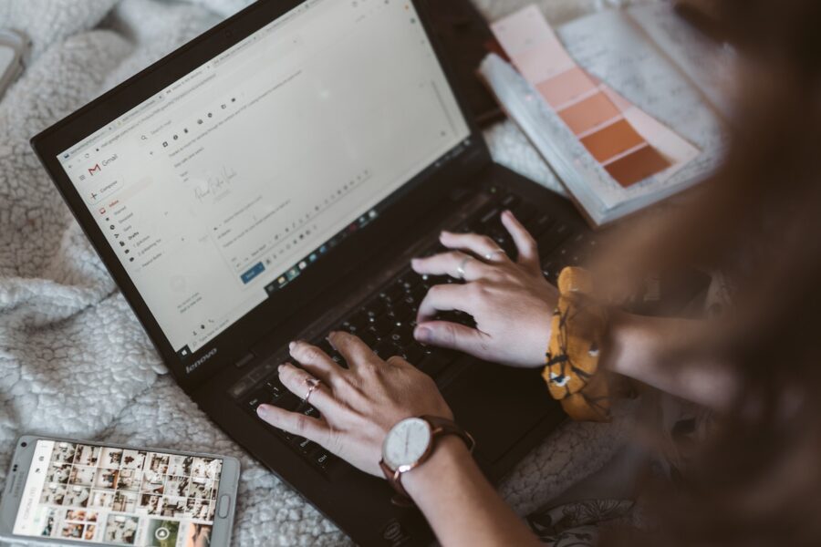 marketer designing emails on a laptop with a cell phone next to her